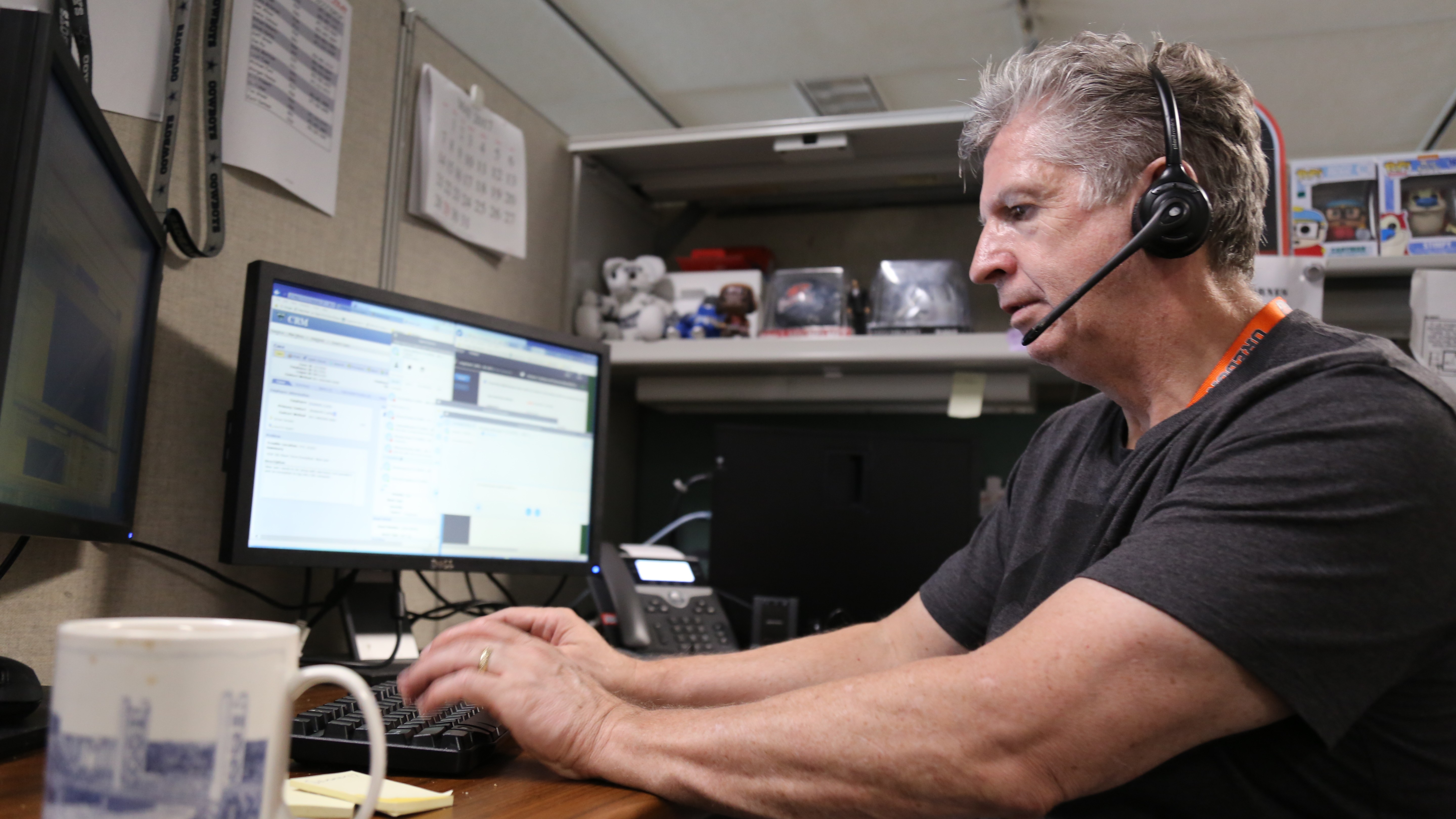man with a headset on, sitting at a desk, looking at a monitor with his hands on a keyboard