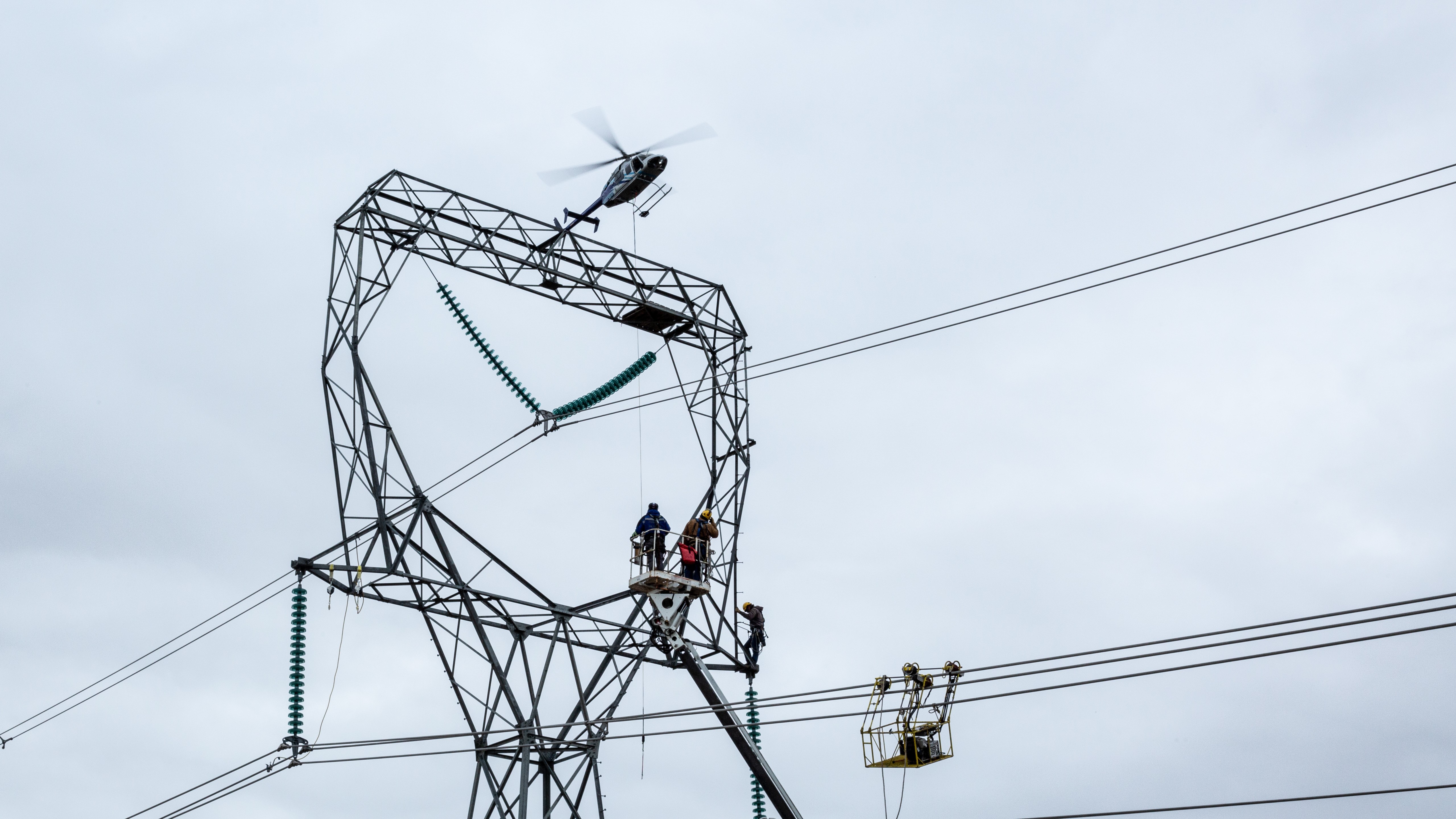 transmission tower, with men standing on it in the distance, with a helicopter overhead