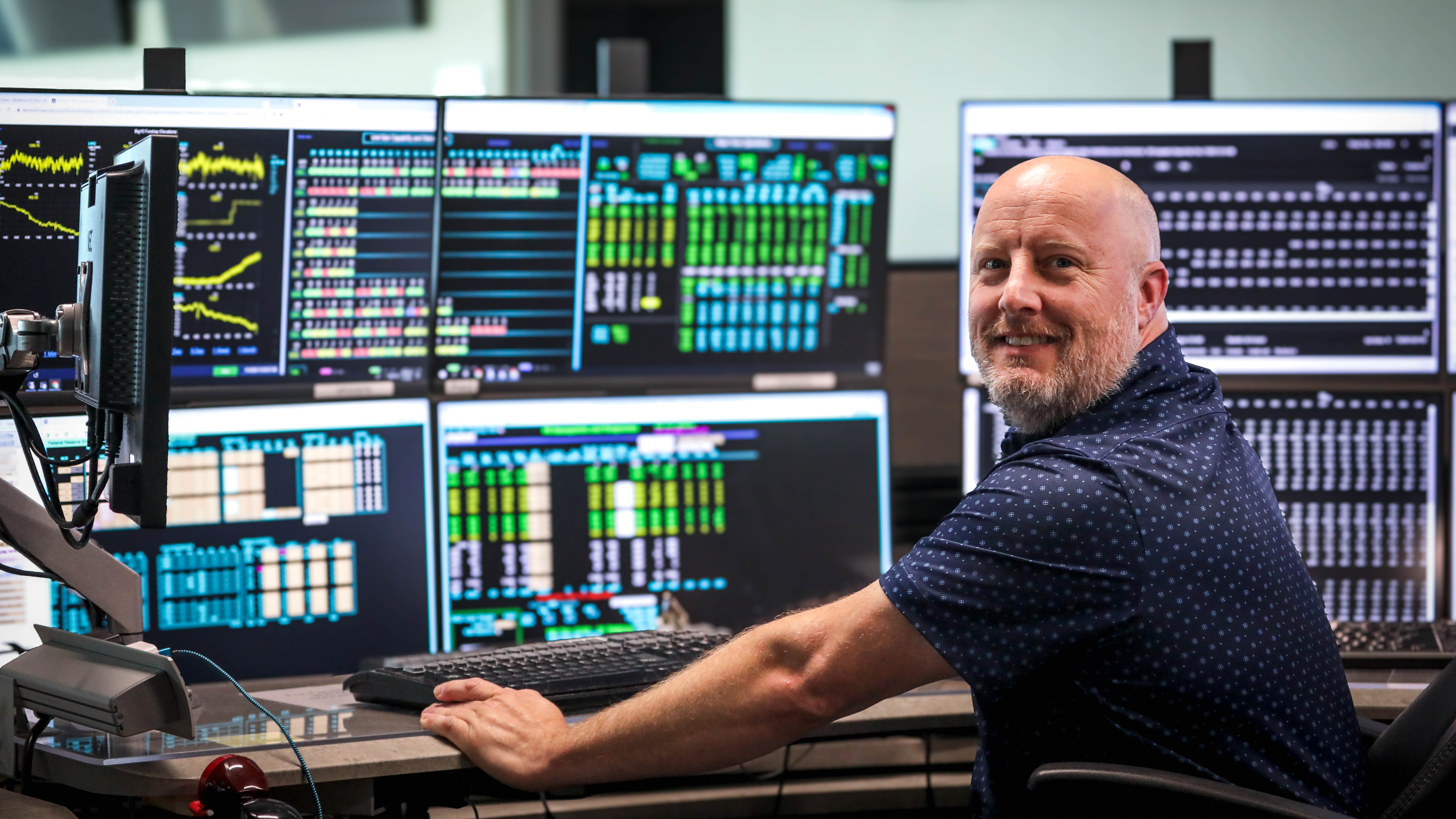 man sitting at a desk, with multiple monitors, turned toward the camera and smiling