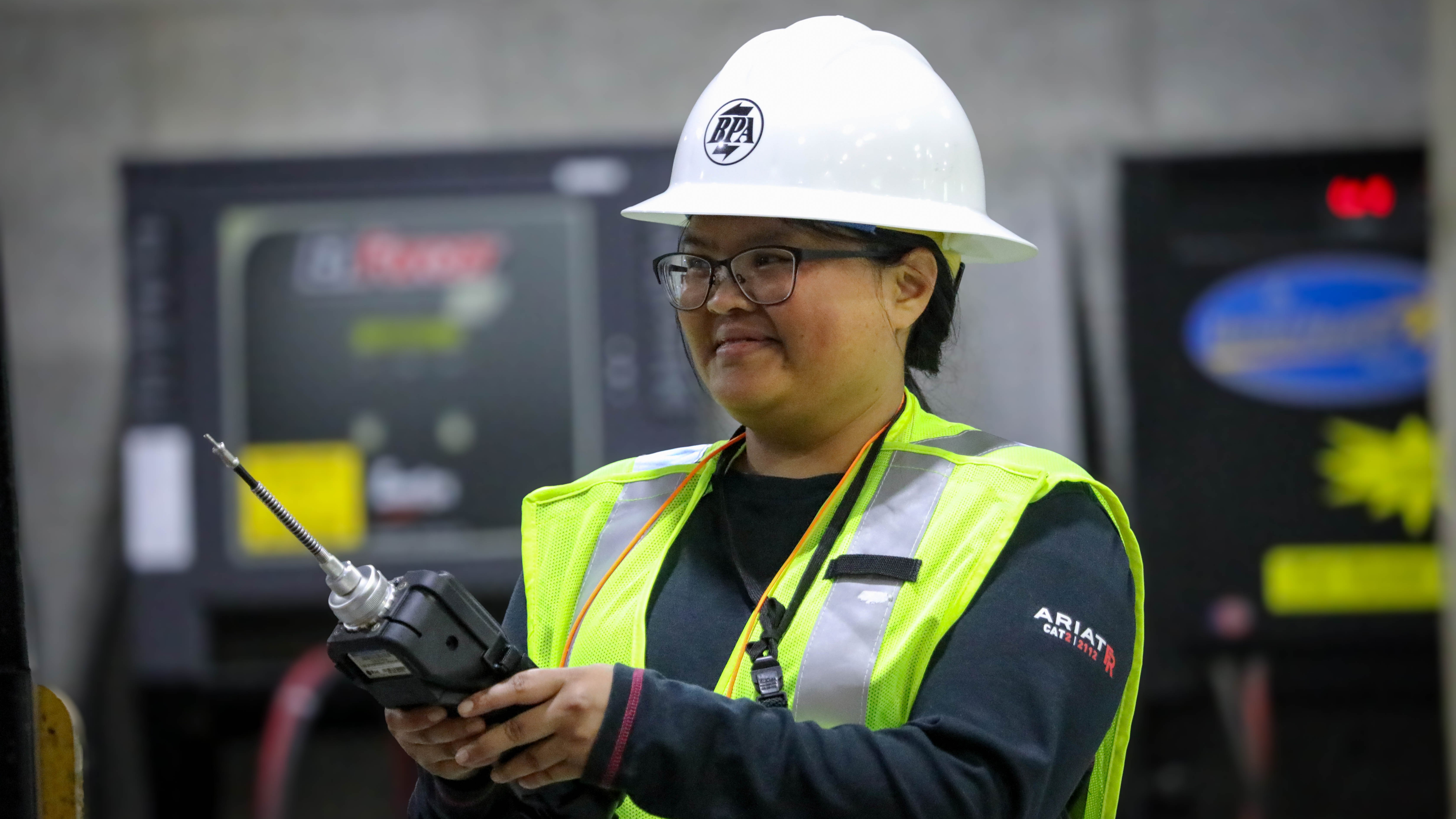 woman  wearing a hardhat and fluorescent vest, holding  a device that looks like a large remote control