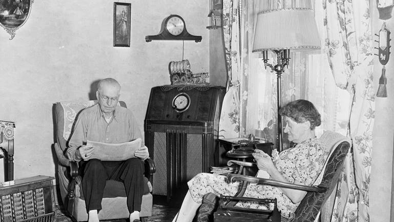 picture of an older man and woman sitting in a living room, enjoying electric appliances like the radio