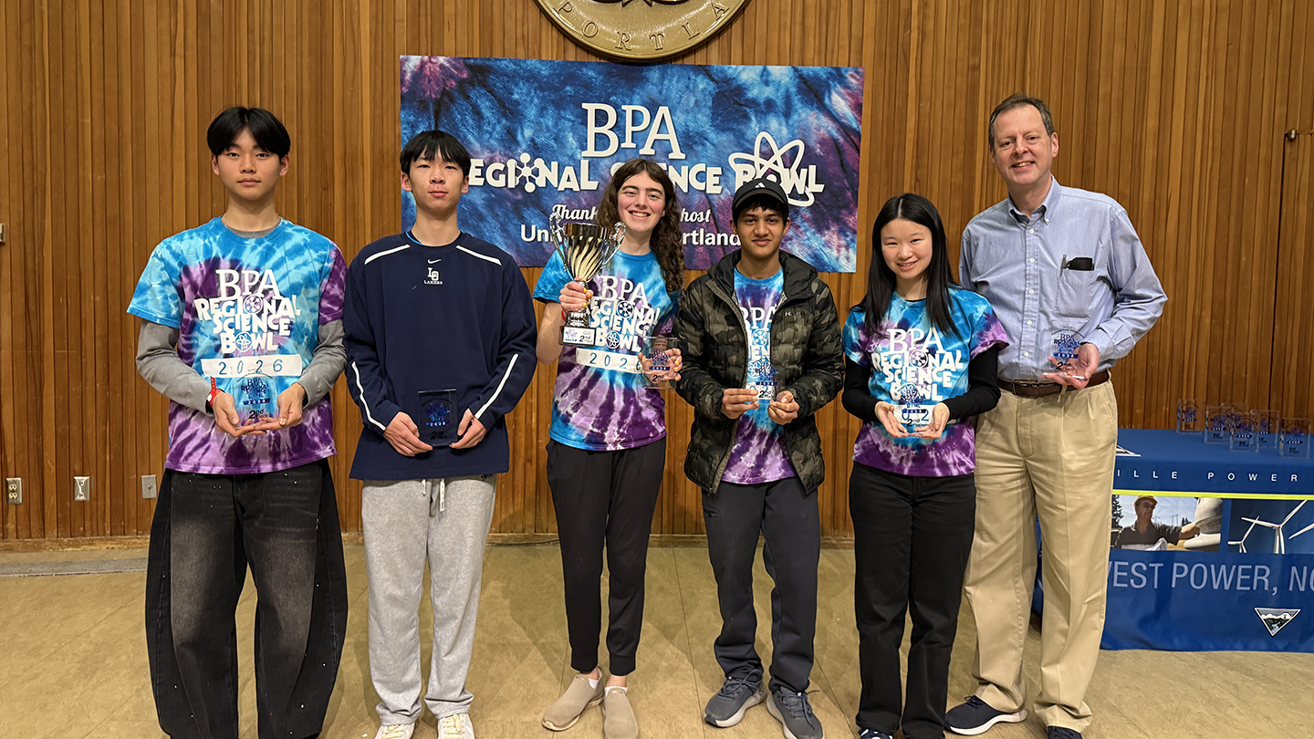 group of people wearing matching science bowl t-shirts, one of which is holding a trophy