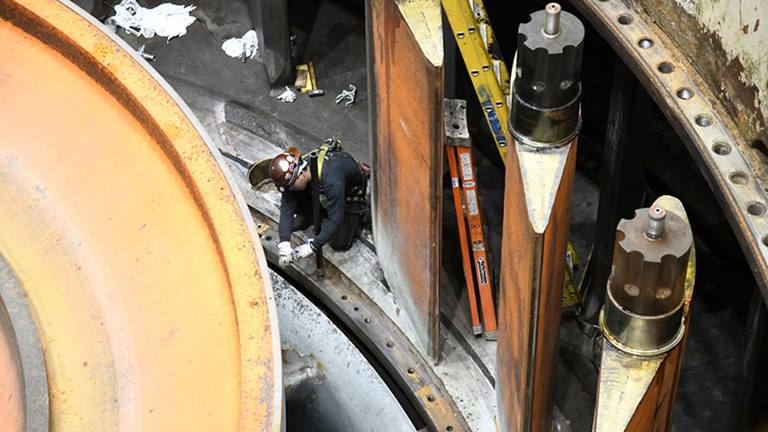 A worker removes the hardware for the wicket gate system on one of three hydroelectric generators at Grand Coulee Dm. Six-and-a-half million pounds of steel was removed from each of the massive units before they were overhauled. Once removed, many turbine components were sandblasted, welded, ground, polished and then repainted before reassembly. Photo by Bureau of Reclamation