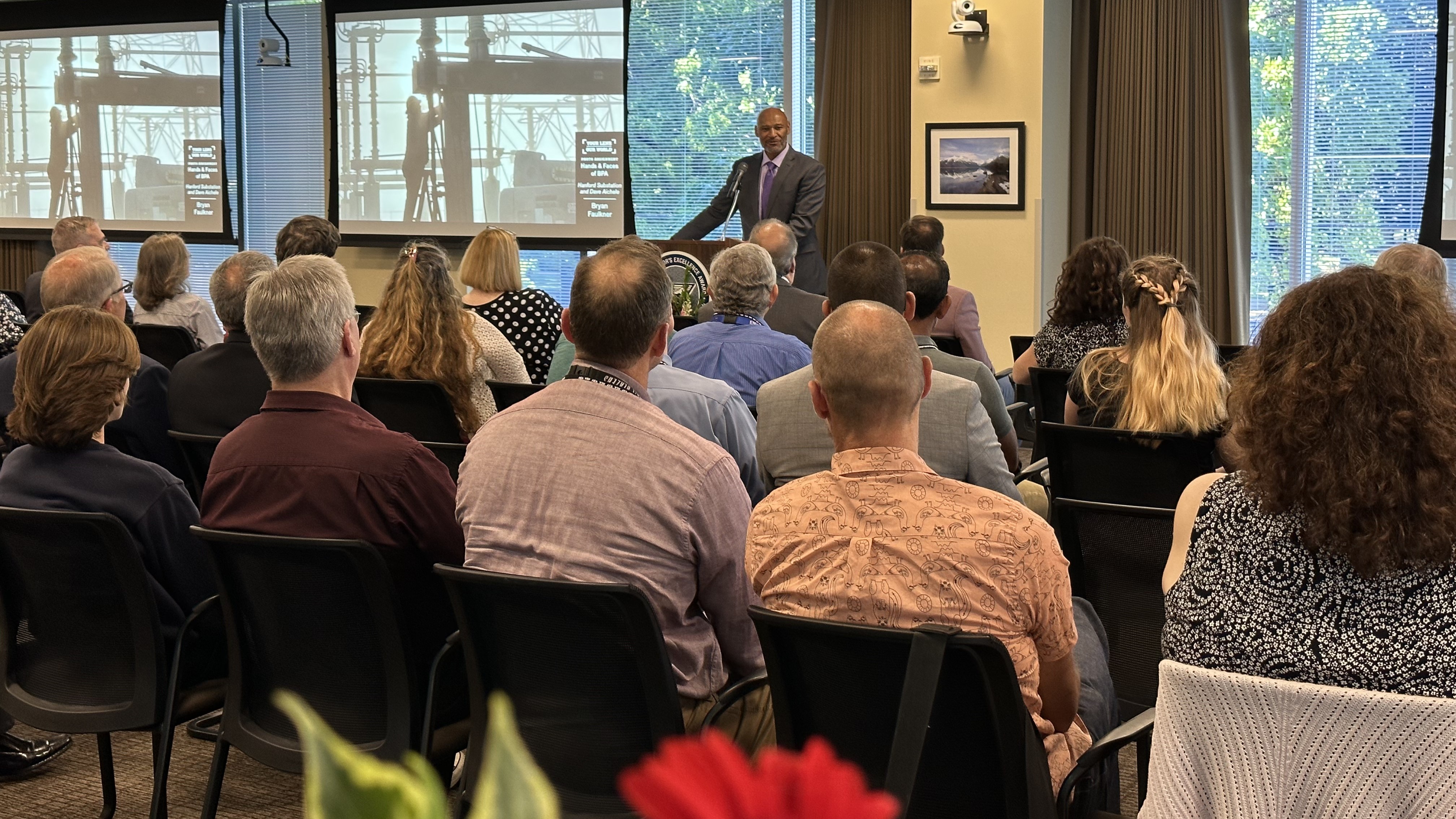 people sitting in a conference room looking at a screen and a person talking in the front of the room