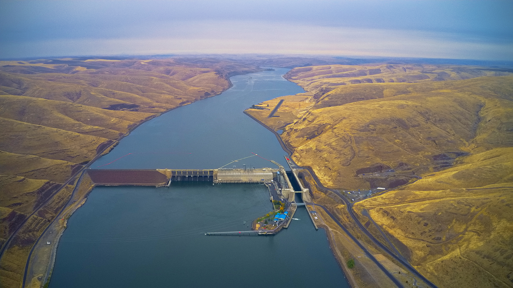 river stretching onto the horizon with olive colored hilly terrain to either side and a concrete structure spanning the water in the foreground